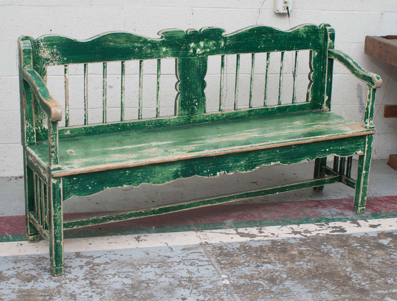 A sturdy, comfortable and attractive pine bench or settle featuring a scalloped and spindled back, shapely arms, scalloped frieze and stretcher base.  Layers of old green paint are rubbed through to the original white and to mellow polished bare