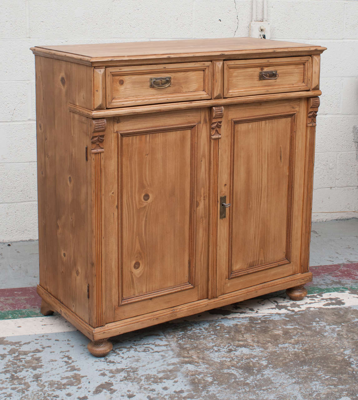 A charming dresser base, a little taller than most, featuring two hand-cut dovetailed drawers above two wide-swinging doors which are flanked and divided by reeded molding capped with corbels.  Remnants of old red paint give this piece a