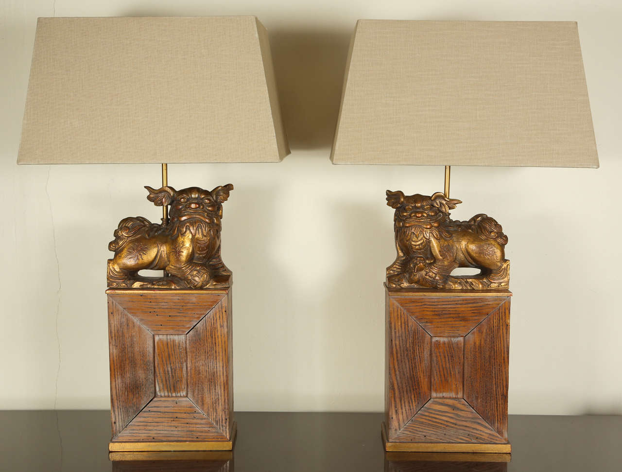 Pair of Stunning foo dog lamps by James Mont.  The slightly distressed oak bases which have a honey colored and gilded finish too them, feature carved wooden Foo Dogs with a gilded finish.  The rectangular shades perfectly compliment the lamps.