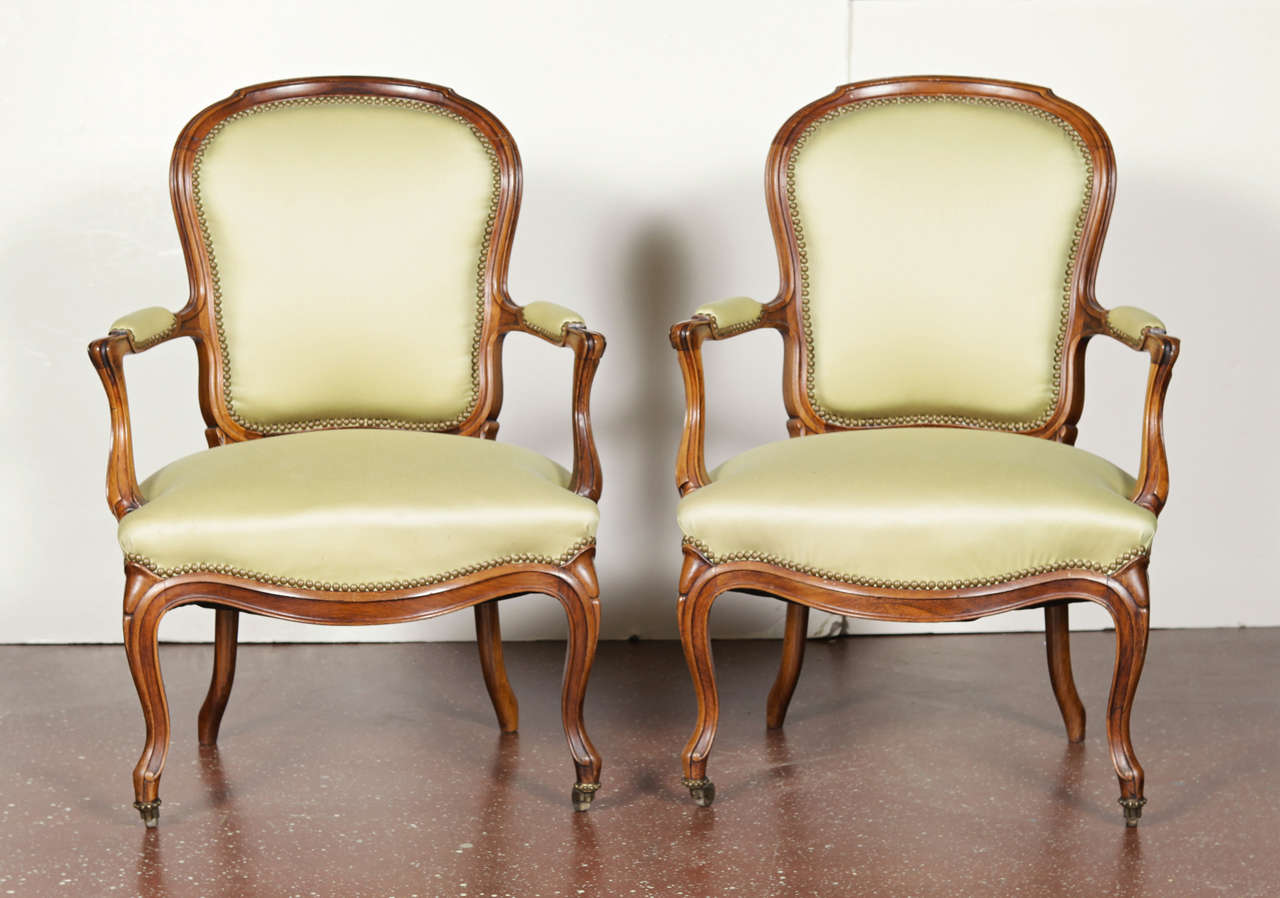 Pair of walnut Louis XV style armchairs upholstered in chartruese wool with nailhead trim.  Casters on front legs.