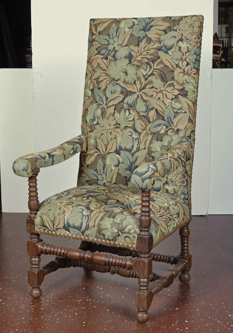 Louis XVIII style tall-back armchair upholstered in green and blue tapestry fabric.  Arms are upholstered.  Nail-head trim and turned legs.