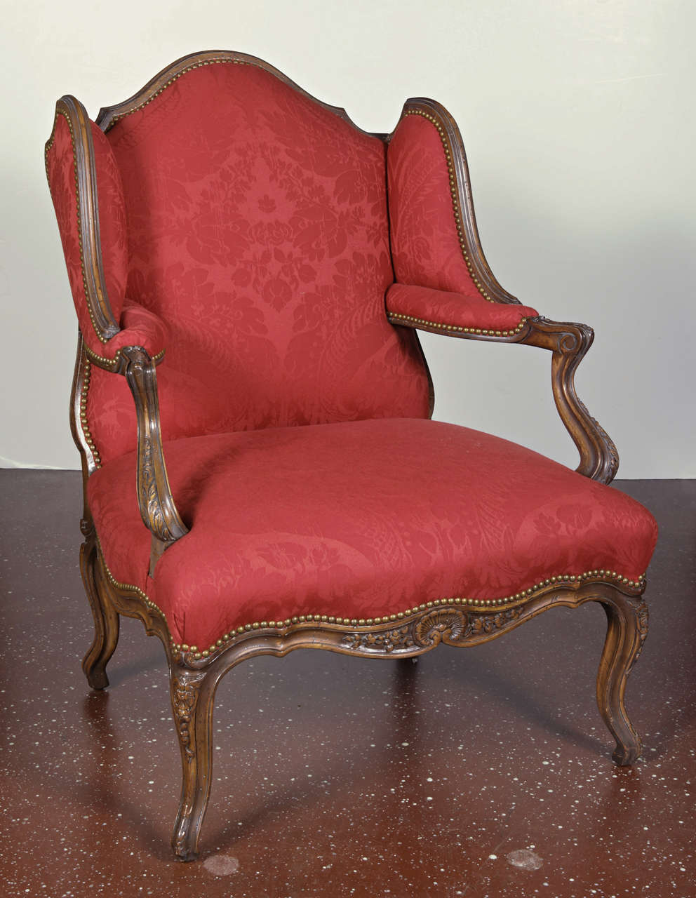 French Provincial style wing-back fauteuil upholstered in red wool damask, with nail-head trim, raised on cabriole legs.