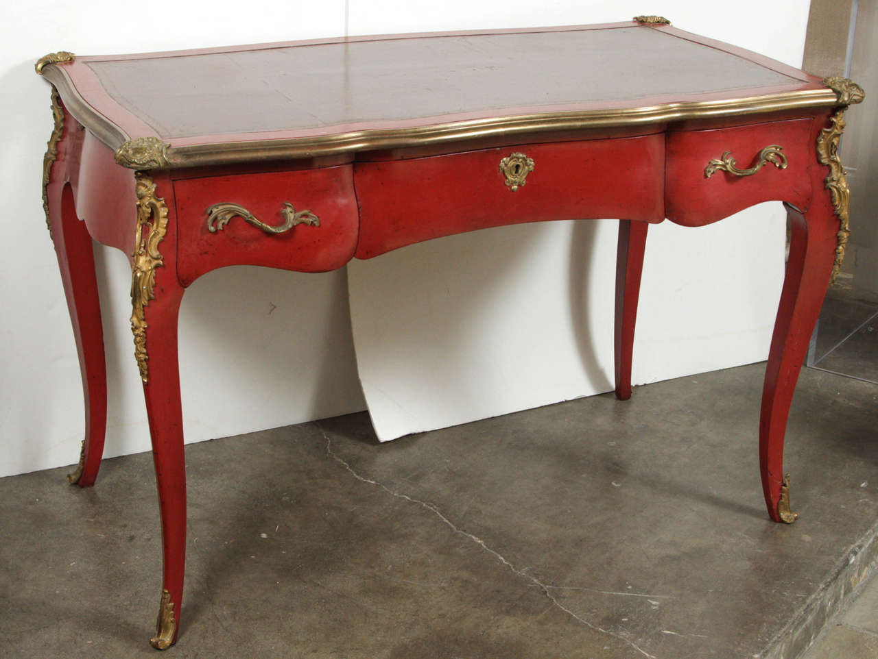 Lacquered, crimson, three-drawer, serpentine desk with ormolu lip, handles and embellishments and hand-tooled, leather top.