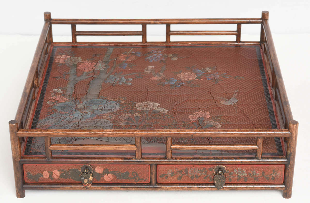 Chinese, Qing dynasty, 19th century. A bamboo and hardwood tea tray of square form having a bamboo gallery to top, the platform decorated with red lacquer having a floral landscape scene to lower left extending toward upper right with birds to