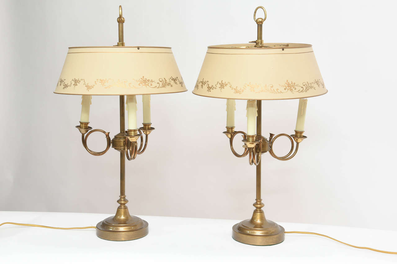 A lovely pair of brass horn motif three-light lamps with cream and gold tole shades.