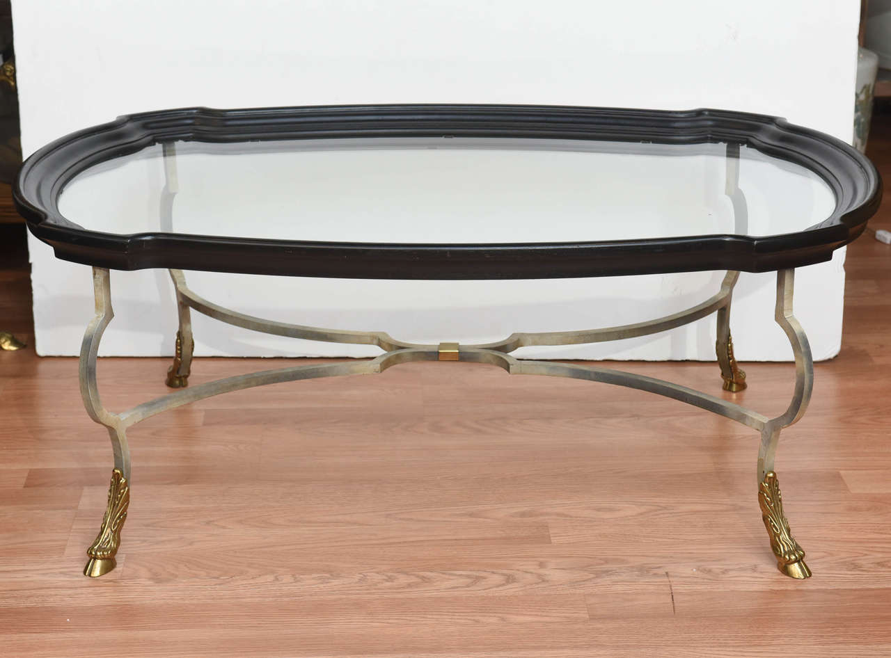 Handsome hoofed foot steel and brass coffee table with a fixed glass wood trimmed tray top.