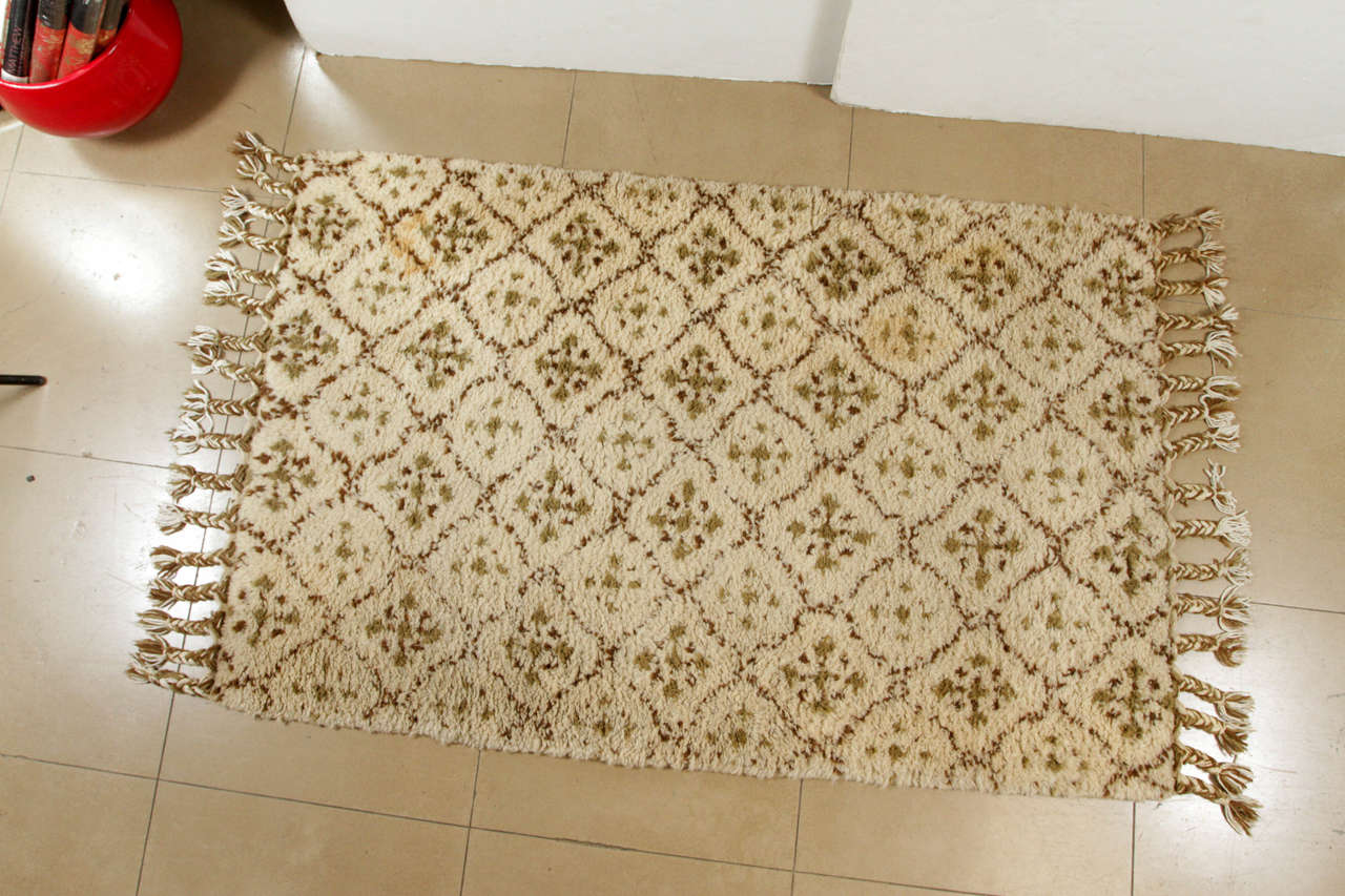 This soulful rug was hand-knitted in Morocco from authentic wool into a repeating diamond pattern with braided fringe detail. The natural rug with variations of beige and brown has a low loop pile ideal for high traffic areas.