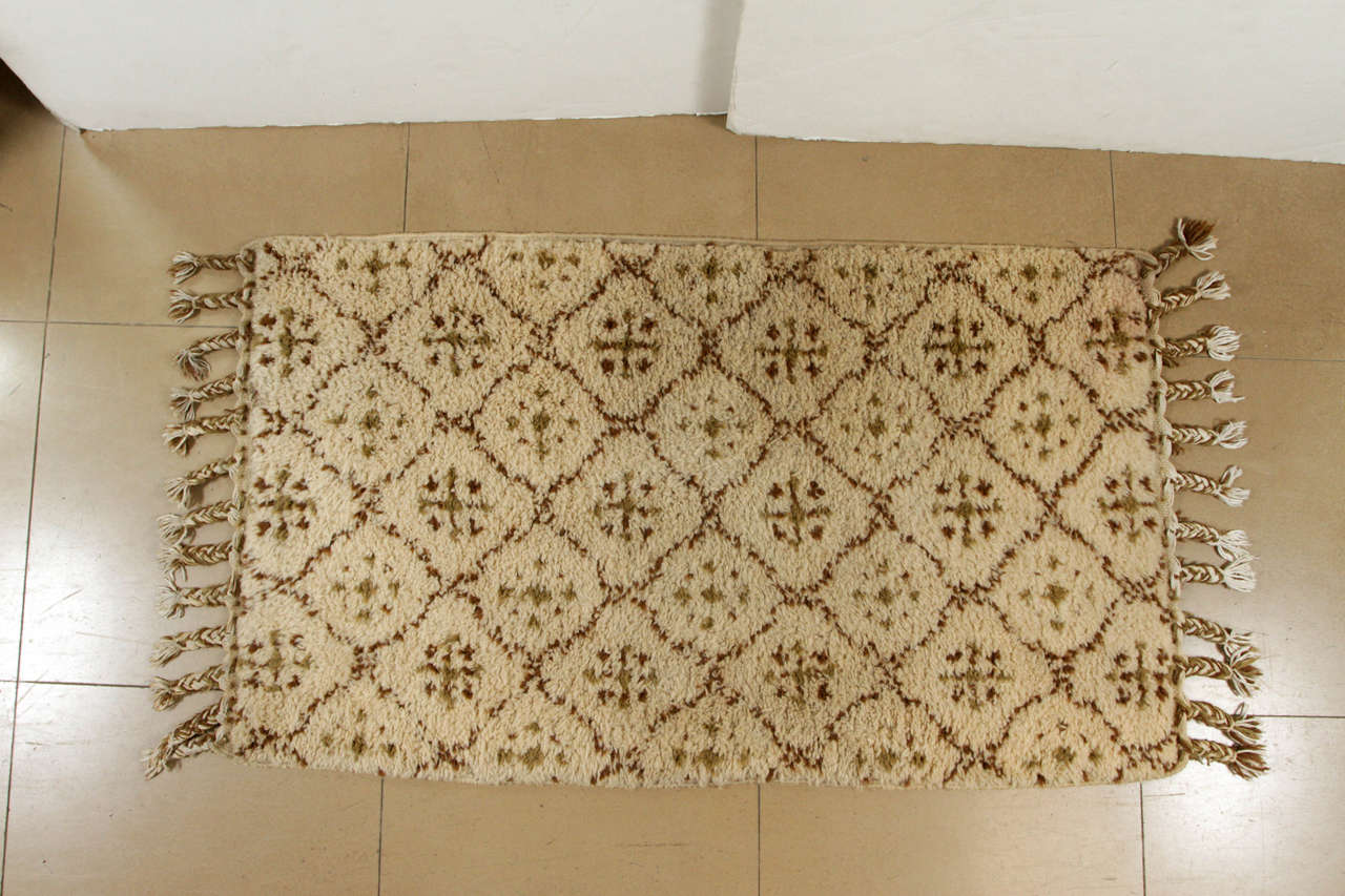 This soulful rug was hand-knitted in Morocco from authentic wool into a repeating diamond pattern with braided fringe detail. The natural rug with variations of beige and brown has a low loop pile ideal for high traffic areas.