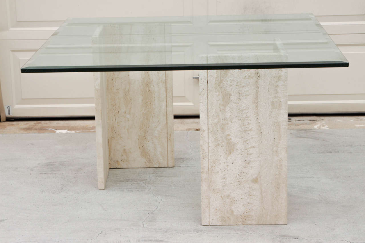 Square glass and pedestal table supported by two L-shaped travertine elements. The two pieces can be adjusted creating a customizable design. Pictured the L-shaped components are separated creating a modern and sculptural table but the elements can