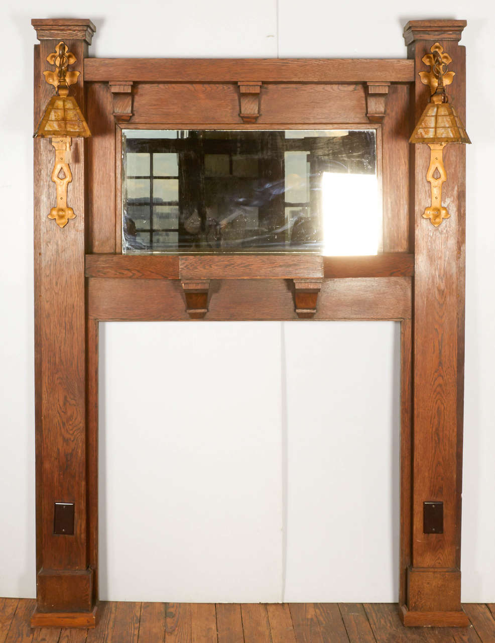 A stunning early 20th century Arts and Crafts style fireplace mantel having integral mirrored overmantel with silvered glass.  Original side sconces have decorative mounting plates and slag-glass shades. Corbel brackets support the three-sided shelf