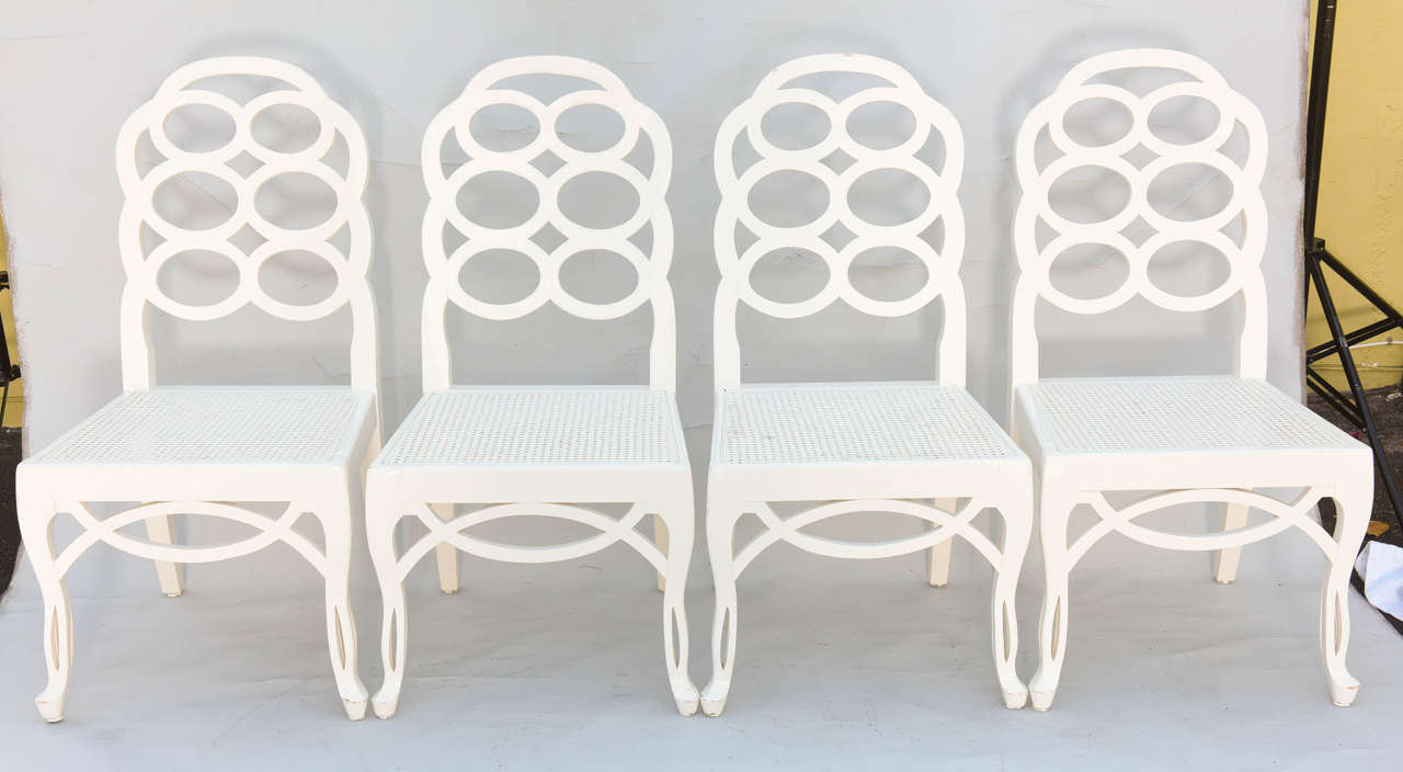 Set of four side chairs, each having a lacquered finish, its back of looped rings, on caned seats, raised on pierced splayed front legs, with looping apron.