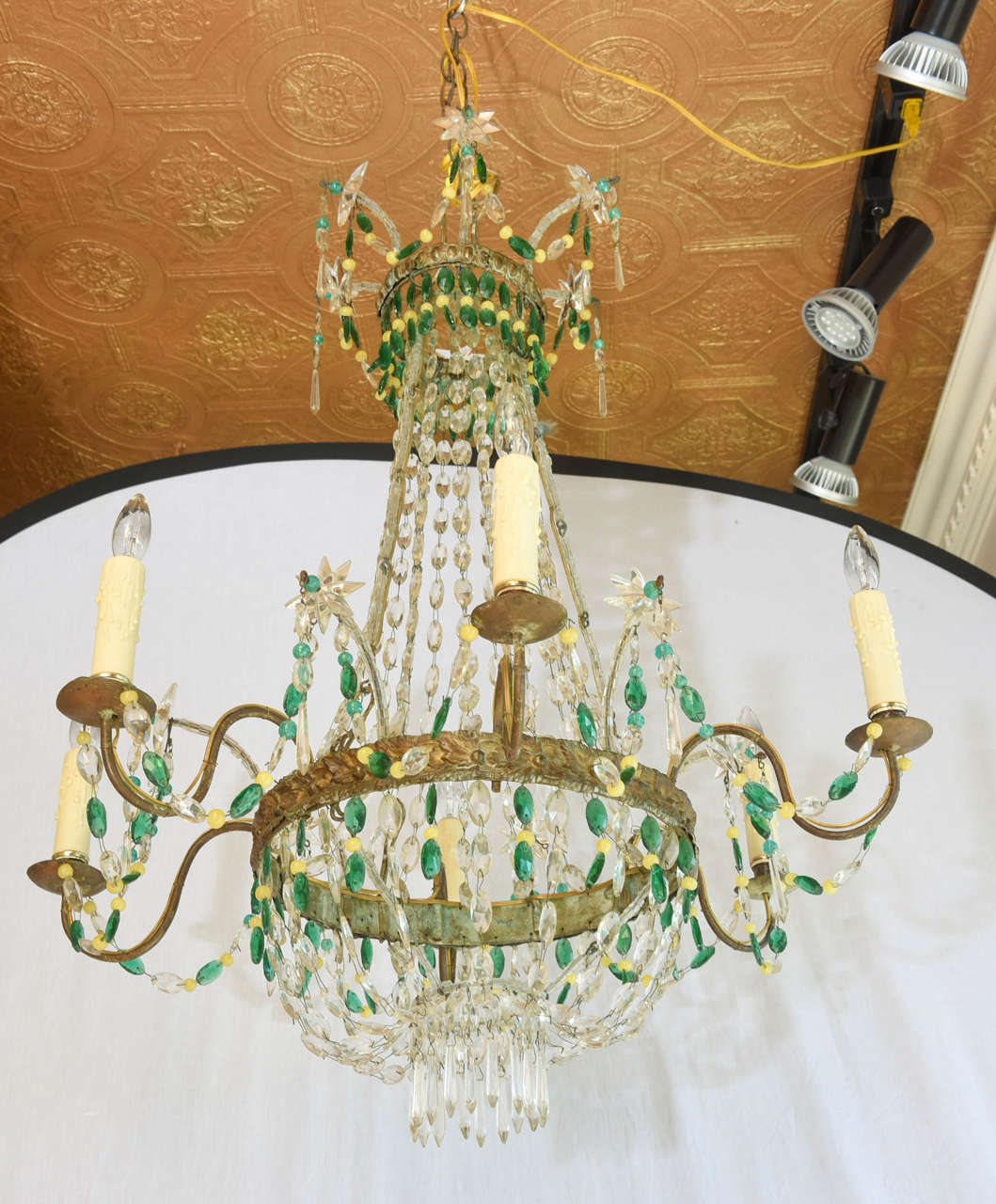 Unusual chandelier, having six-lights on S-scroll gilded iron candlearms, affixed to repousse band, hung from swagging strings of faceted oval crystals, finishing in a basket, surmounted by two-tiered crown, decorated with whimsical starburst