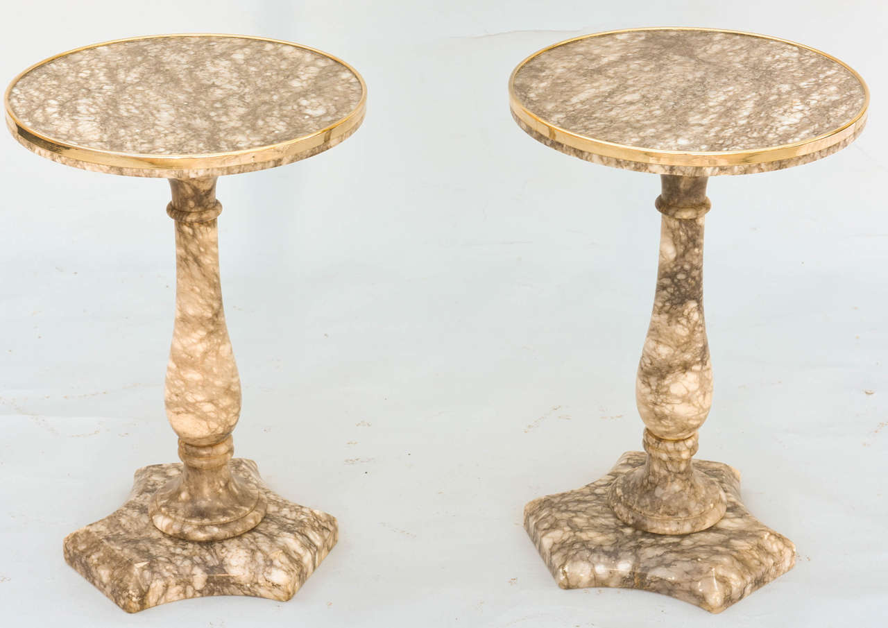 Pair of tables, of alabaster, each having round top with brass trim, raised on pedestal with tripartite base.