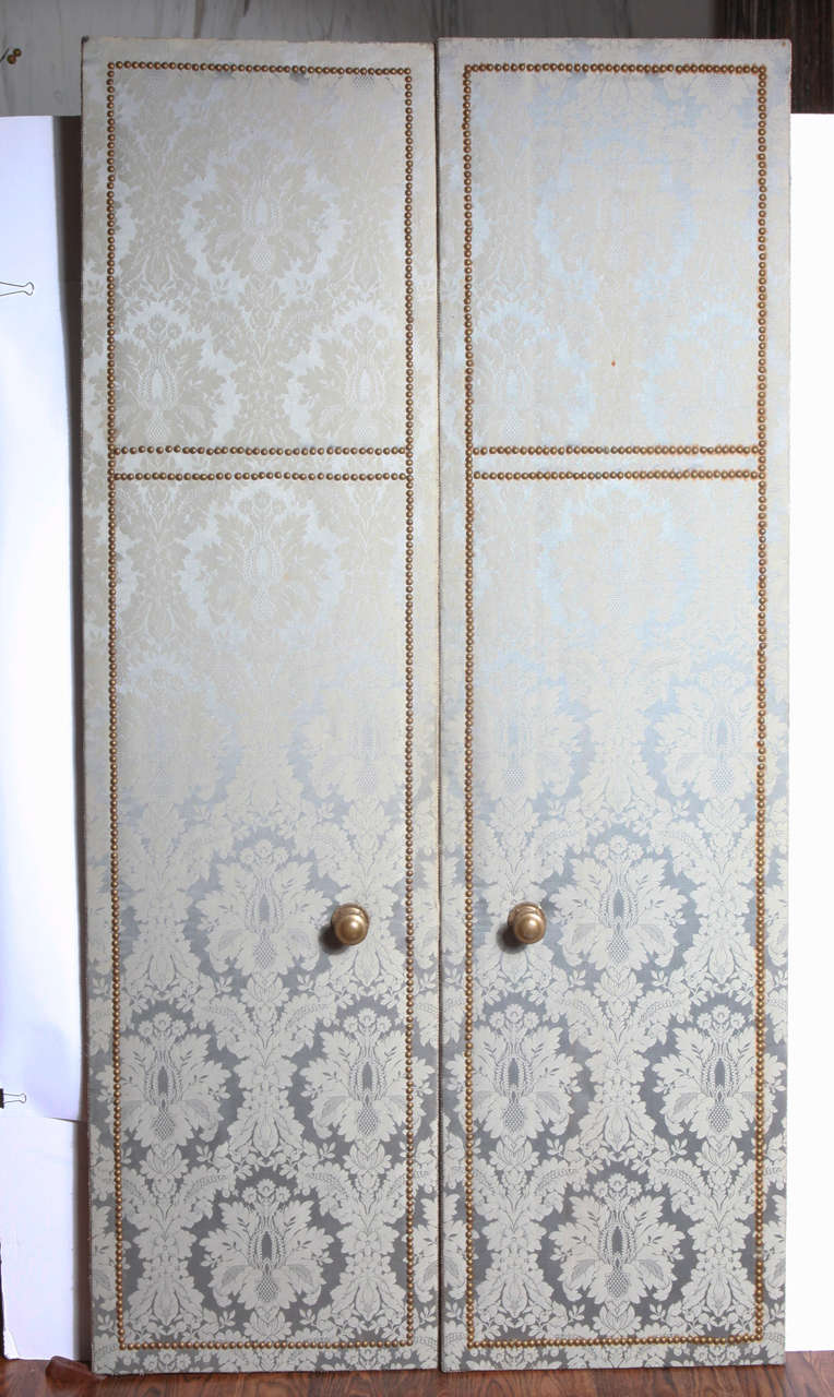 Pair of small, decorative damask doors feature brass nailhead and large bronze knobs.