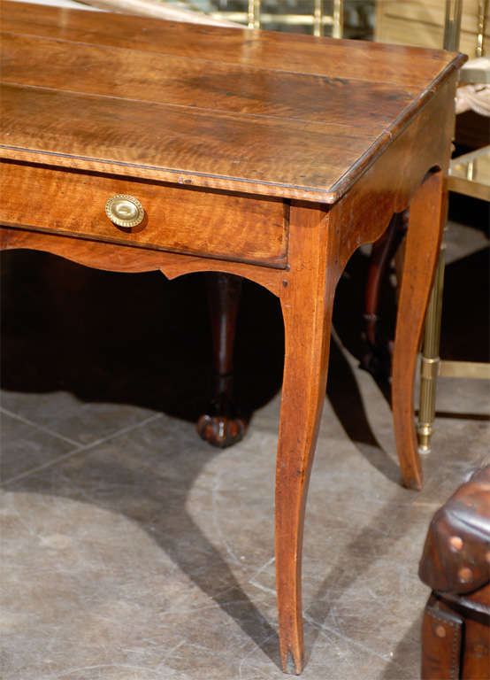 A French Louis XV style walnut desk with single drawer, scalloped apron and cabriole legs from the early 19th century. This French 1820s writing table features a three-plank rectangular top with beveled edge over a long single drawer with brass