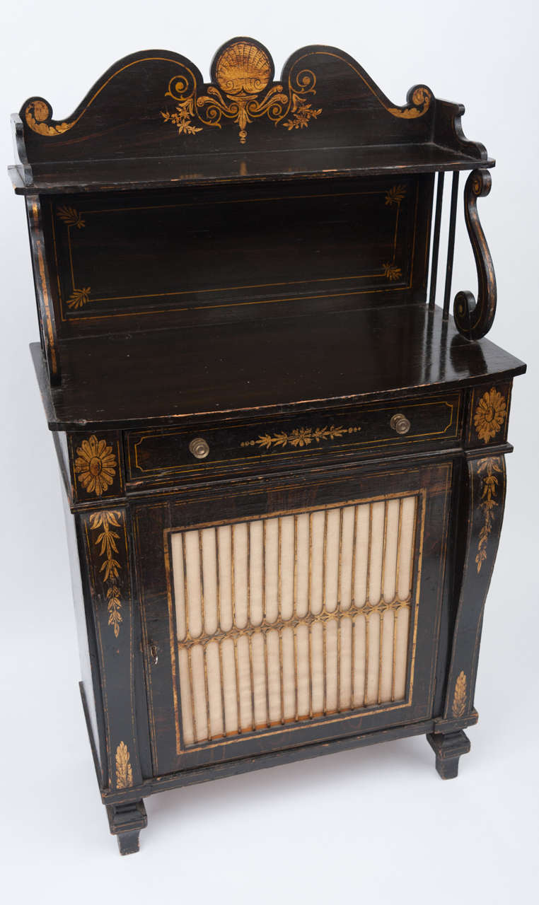 Regency black and gilt decorated chiffonier of small proportions.  The shaped superstructure with 's' scroll supports terminating on the bow fronted top, with frieze drawer below.  The single door with brass grille flanked by scroll supports on