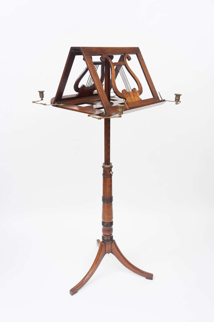 A good Geo III mahogany duet music stand. The twin lyre music supports with original adjustable brass candle sconces on a telescopic column, the three swept legs with ebony stringing. Measures: 16½ wide, 43½ high.
