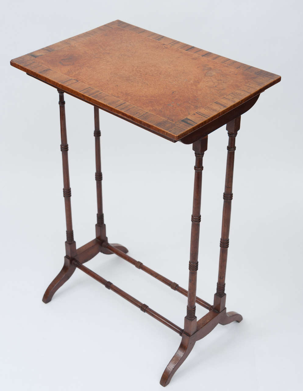 An unusual and elegant Regency occasional / end table.  The top and its edge both veneered in burr elm; with wide rosewood cross banding.  Raised on slender turned twin end supports with scroll feet and turned stretchers.  Lovely colour.