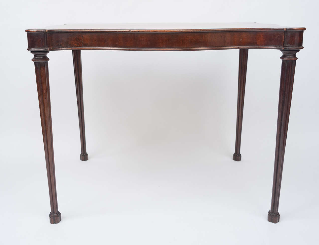 A Geo III mahogany silver table of unusual serpentine form, the moulded top above a crossbanded frieze. Raised on very elegant cluster-column legs with cinquefoil block feet.