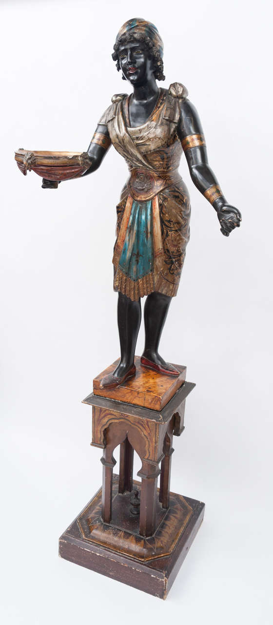 A good C19th Venetian blackamore torchere.  The female figure, with original polychrome and silvered decoration.  Her pretty face with carved curly hair and striped head dress and her flowing robes with bright decoration and tied with a waistband