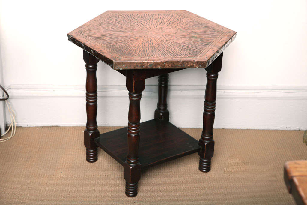 English Arts and Crafts table, the hexagonal hammered copper top with radiating star detail, hammered etched banding, over balustrade turned legs joined by lower shelf, standing on ring turned feet.