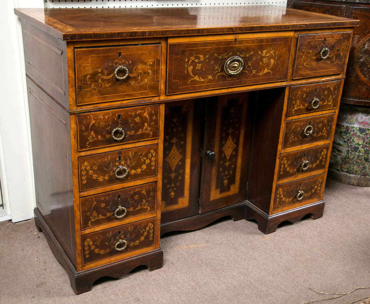 This desk is of light colored mahogany with inlays of swags, vines and leaves in satin wood or other very light wood.
The top is banded in a 1.5 inch wide band of hand done pen work on satin wood, bordered by ebony.
Four drawers on either side