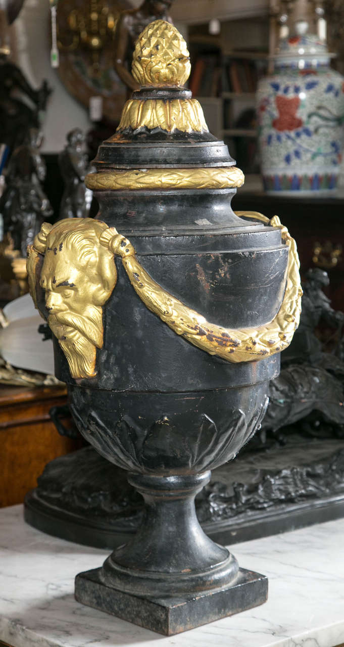 In the classical style, this pair has an acorn finial above acanthus leaves and ring. Satyr masks, connected by swags on either side. Leaf form bottom to body of urns, raised on plinths. The lids are removable.
The gold leaf, we believe, has been