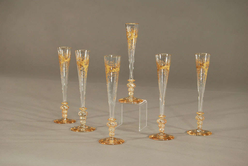 An exquisite set of 6 tall and elegant hand blown champagne flutes with elaborate bases. These are decorated with 2 colors of raised paste gold with scrolls and leaves and they invite you to raise your glass in celebration! The base and rim is also
