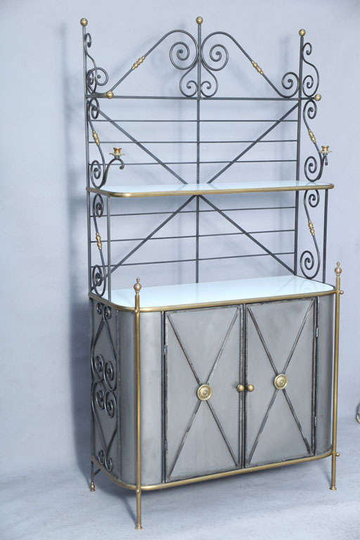 Baker's rack, having two shelves in graduating-size of milk glass, over polished steel base with two cupboard doors decorated by X-frames centered by a brass rosette; its sides and shelves supported by iron scrollwork trimmed in brass accents.