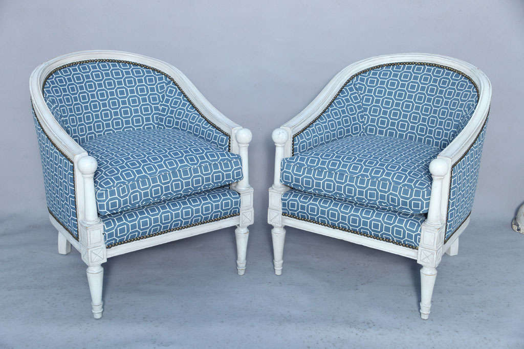 Pair of upholstered bergère chairs, barrel-form with distressed painted finish on channeled frame, each having low sweeping back with arms terminating in ball finials, on turned stiles; loose drop-in cushion, raised on round tapering legs.
