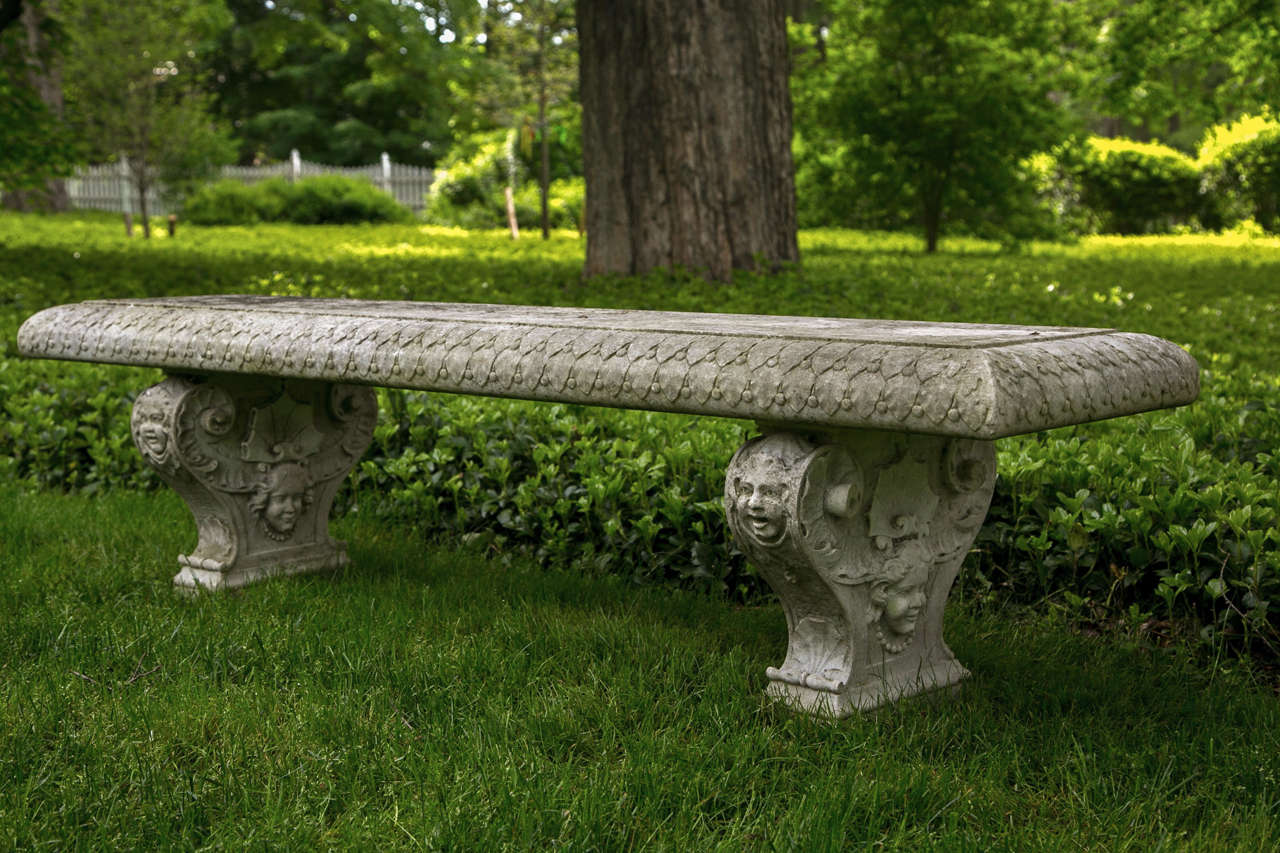 A carved marble bench, the top with foliate motif on rim, the supports embellished with female masks wearing beaded necklaces, shell motifs and volute scrolls.