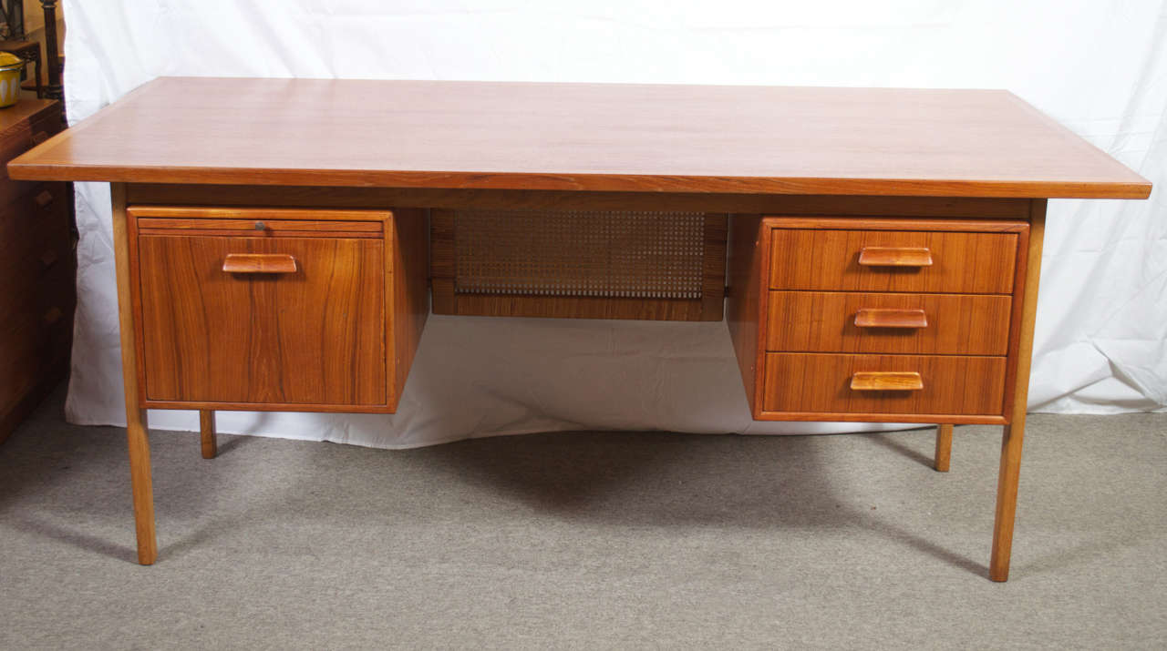 A nice looking vintage Danish executive desk in Teak, with a Rattan modesty screen. Has three drawers on one side the other has a file drawer and a pull out tray, with a large work area on top, this desk gives you the storage and work area to get