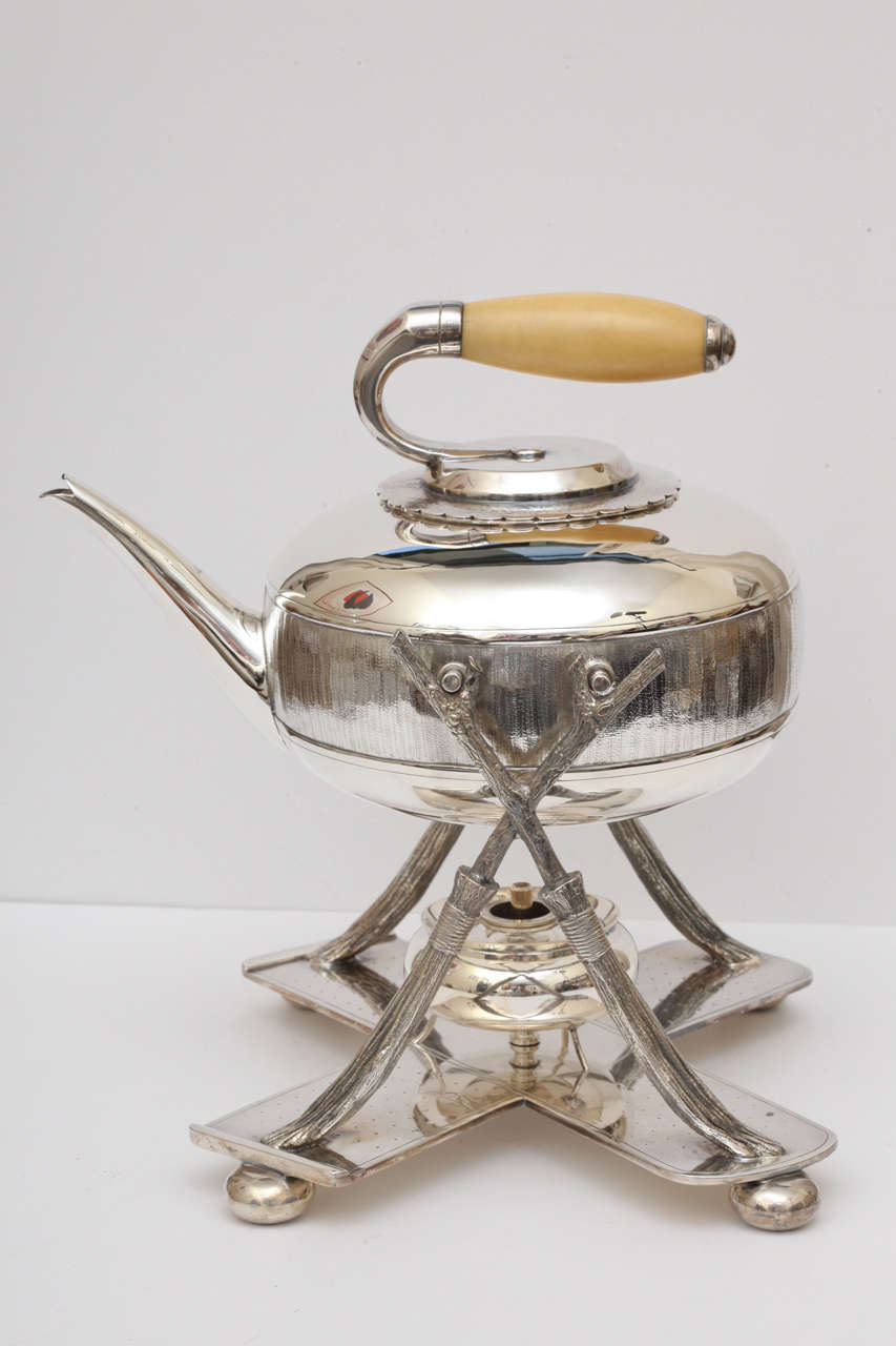 An English silver plated tea pot with warmer and stand. Designed with a curling motif the pot stand is formed by a pair of crossed brooms and the the teapot is designed as a curling stone. A wonderful figurative piece made around the turn of the