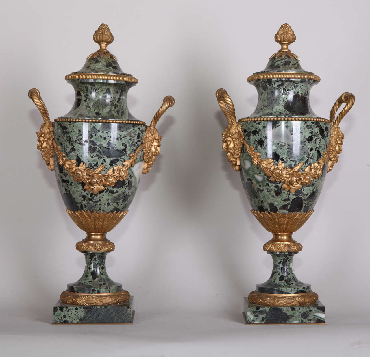 Decorated with mask shaped handles and flowers garlands. The lids with pomegranate finials, on a circular foot raised on a square base.