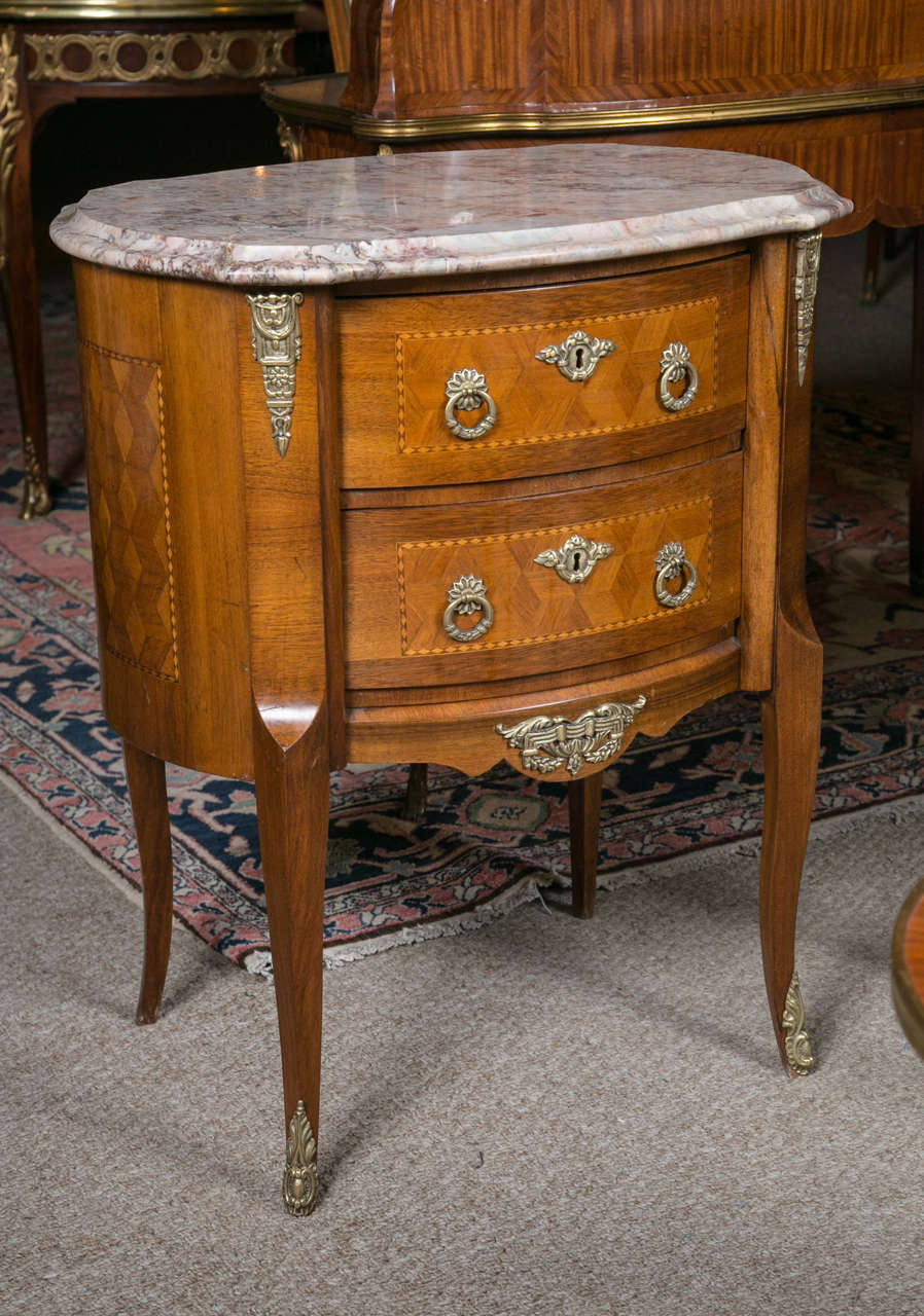 Pair of French marble-top kidney shaped commodes. Exquisite in size and shape - this pair is adorned with unique drape, buckle, flower and arrow side bronze pieces adding distinct character along with the creamy rose veined marble top. These fine