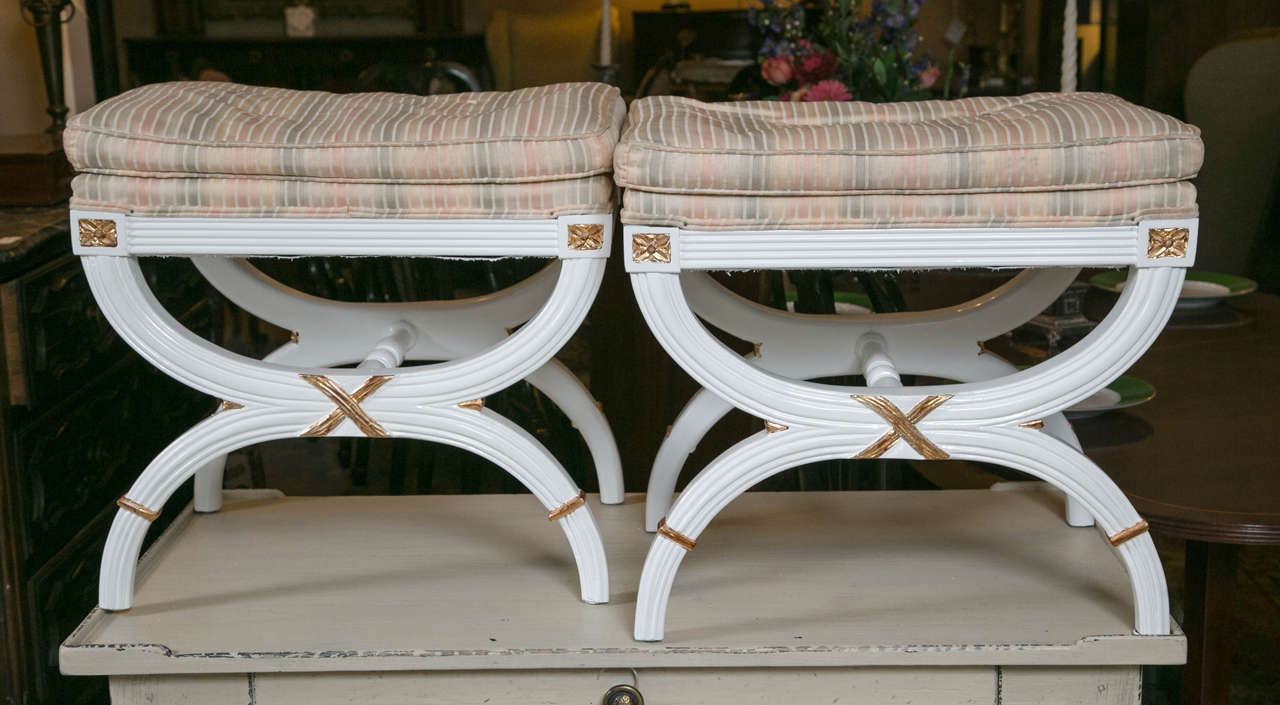 Pair of Hollywood Regency white painted X-benches or footstools. A fine pair of X-benches with gilt gold hi lights finished in a white lacquer. The beauty of these benches will add timeless character to any area of the home/office.