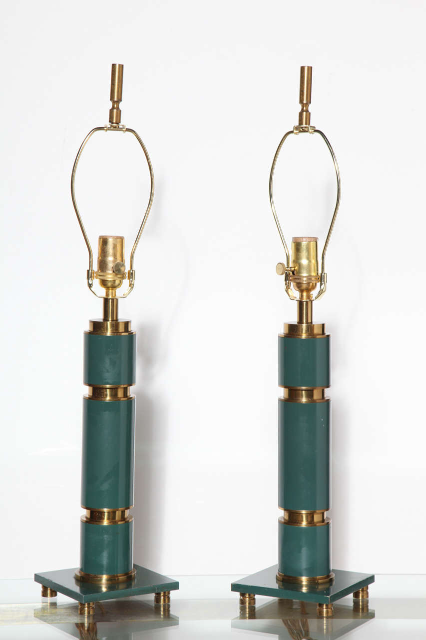 Pair of Hollywood Regency Blue Green Enamel and Brass Lamps in the manner of Walter Von Nessen. Featuring a cylindrical stacked Brass and Bluish Green enameled column, square enameled footed base, on round Brass feet with original finials. Three-way