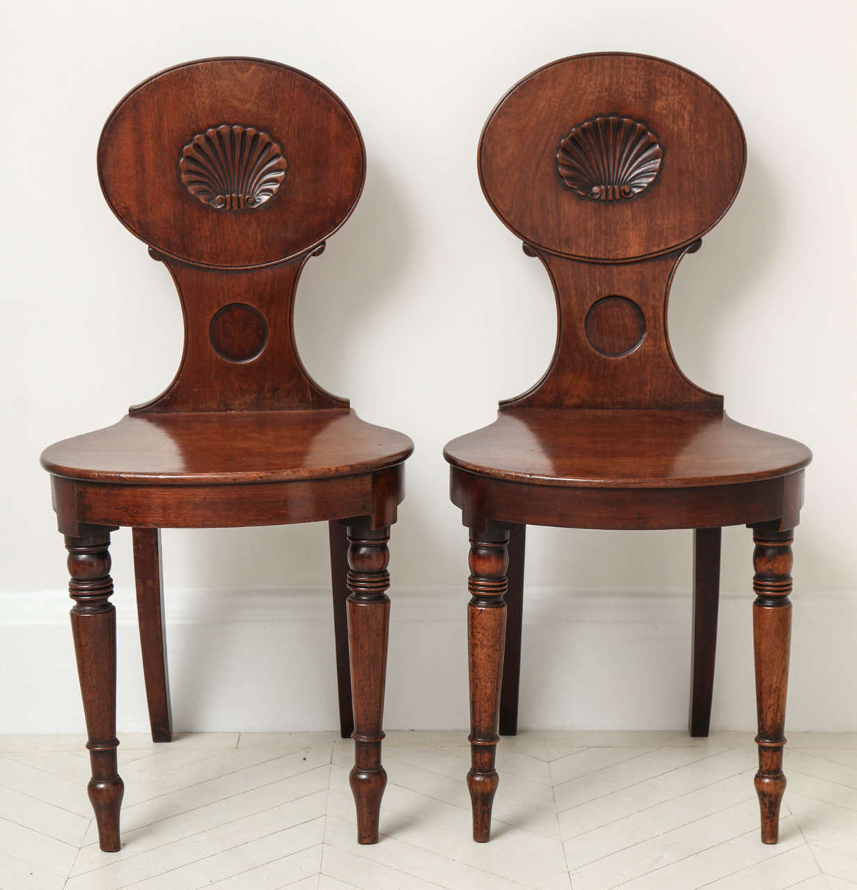 A pair of English Regency mahogany hall chairs with carved shell backs and turned front legs