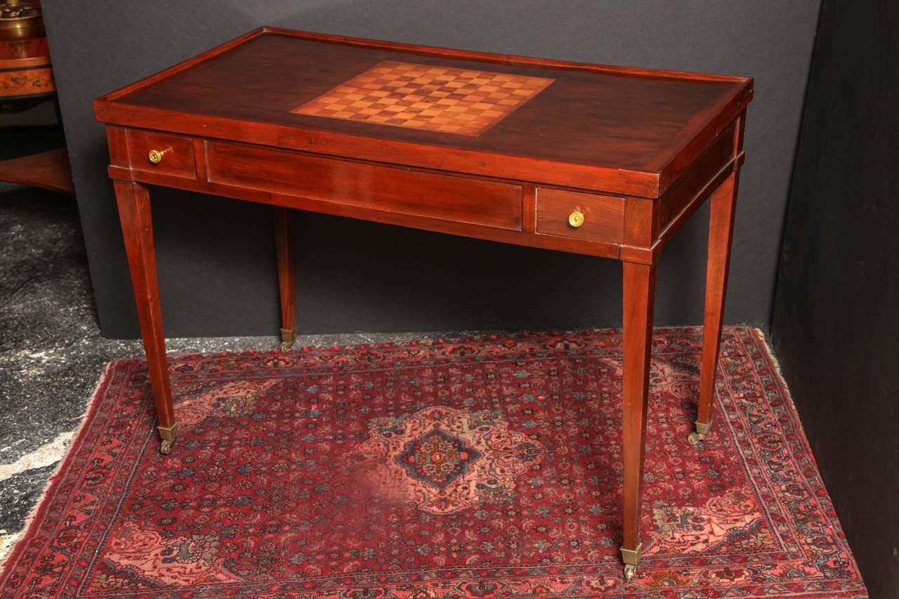 A French Directoire mahogany tric-trac table, the removable top with central inlaid chessboard, the interior with in inlaid backgammon board, the frieze fitted with small opposing drawers, and on tapering square legs ending in brass casters.