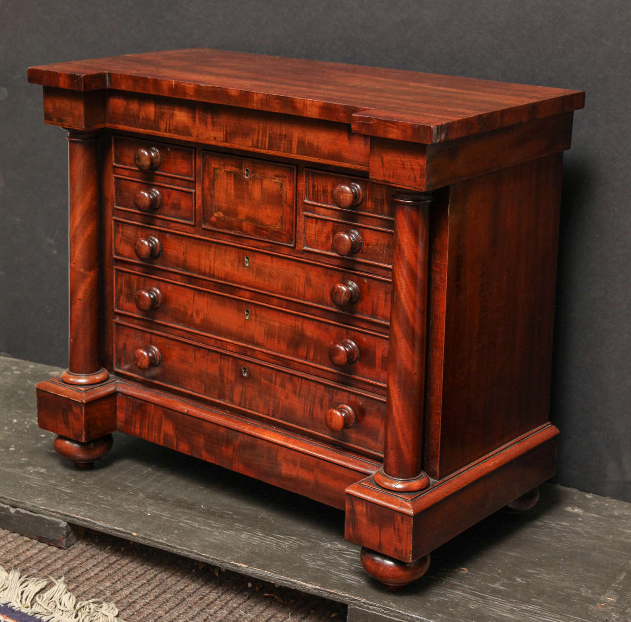 A fine William IV figured mahogany miniature chest of drawers with columns flanking an assortment of small and large drawers, on top-form feet.