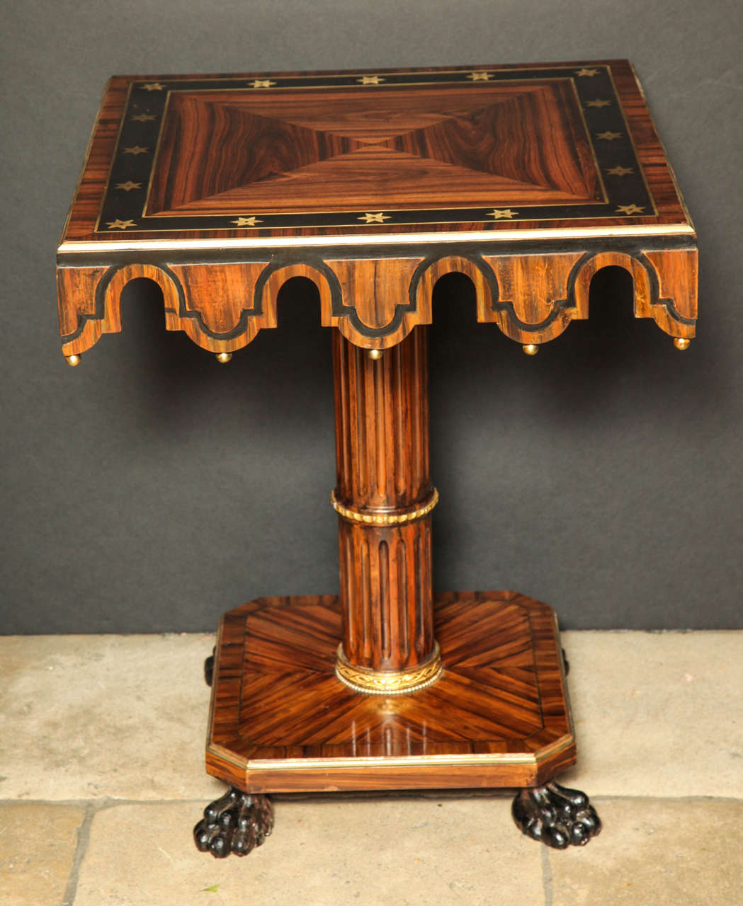 A pair of Regency calamander, ebony and cut brass inlaid square pedestal tables, each top quarter veneered and banded with star-inlaid ebony, unusual crenelated apron and fluted column support resting on paw feet.