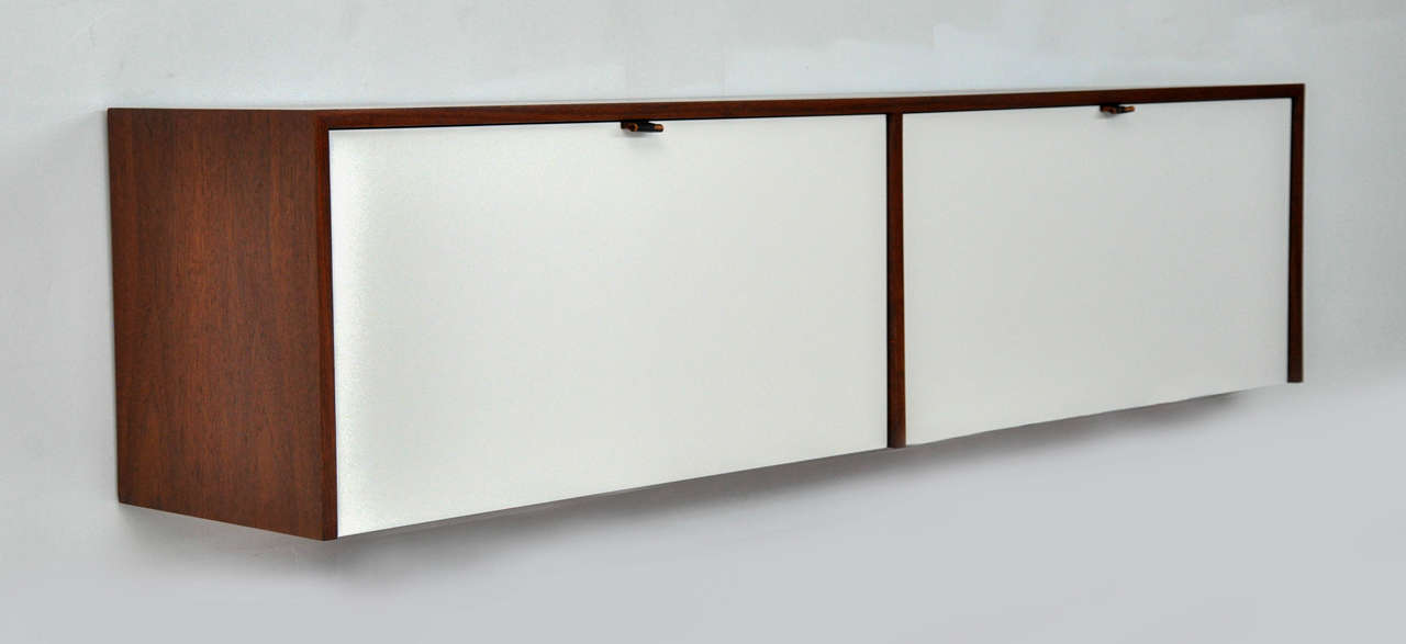 Wall mount credenza by Florence Knoll. Walnut case with white doors and leather pulls. Fully restored.