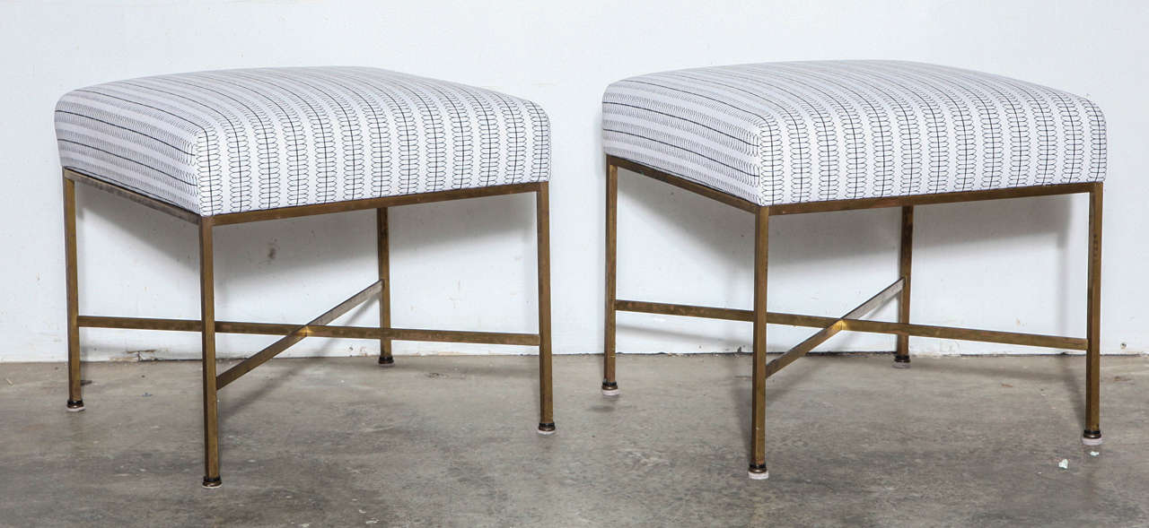 Two elegant Paul McCobb stools newly upholstered in Nate Berkus cotton fabric. Thin ribbon brass stretchers connect square brass legs.