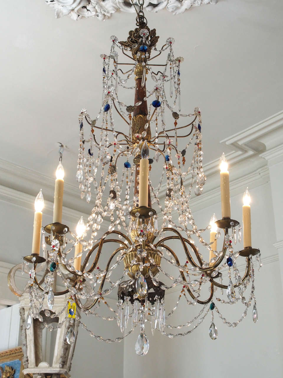 19th century eight lights Genoa crystal chandelier. Three tiers with a bottom tole crown. 
Mostly white crystals but a mixture of blue, red, orange and green crystals. Wood and giltwood center body with eight iron arms. US wired.