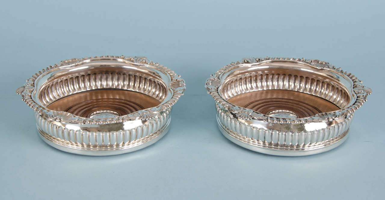 Decorative pair of George III sterling silver wine coasters. 
Maker: Joseph William Story. London 1808. 

The gadrooning on the border is interspersed with shells, surrounded by acanthus leaves which give these wine coasters a very festive air. 
The