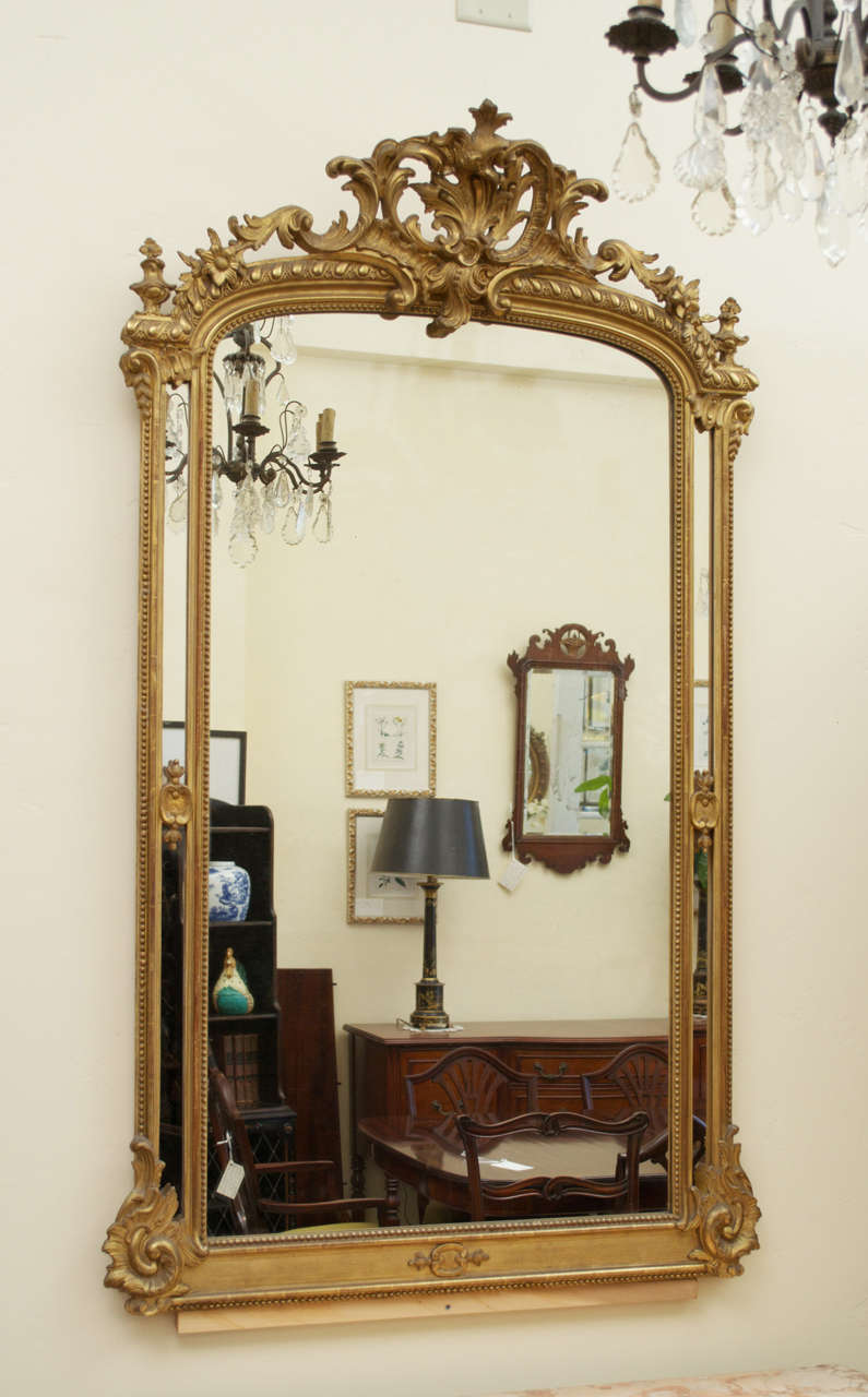 A magnificent double framed, giltwood mirror with carved flowers and foliage adorning the cartouche. Both the inner and outer beaded frames surround the side mirror panels. The richly carved and pierced ornamental crown bows out on top and the