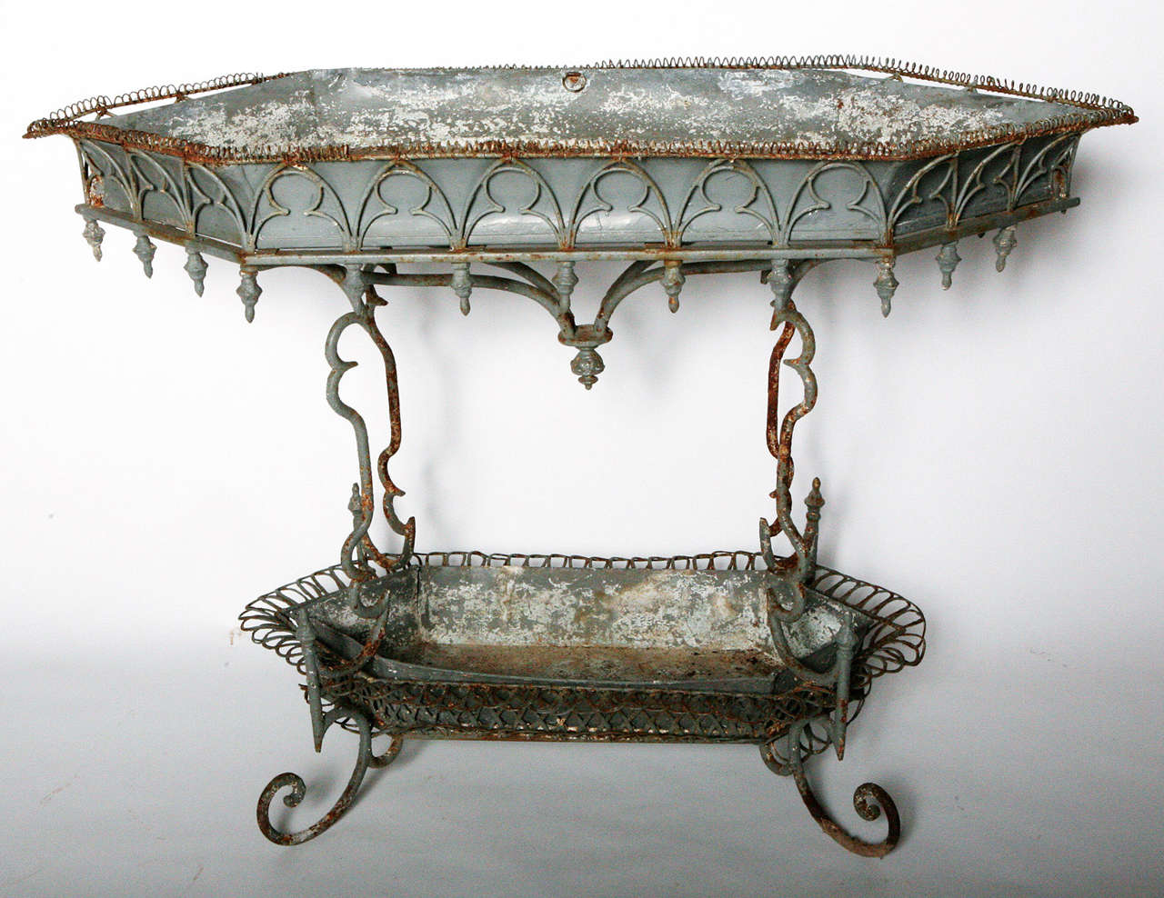 Wonderful two tiered iron plant stand with original liners.  Delicate french wire with gothic design, and gracious curved iron, and finial drops around the base of top tier.