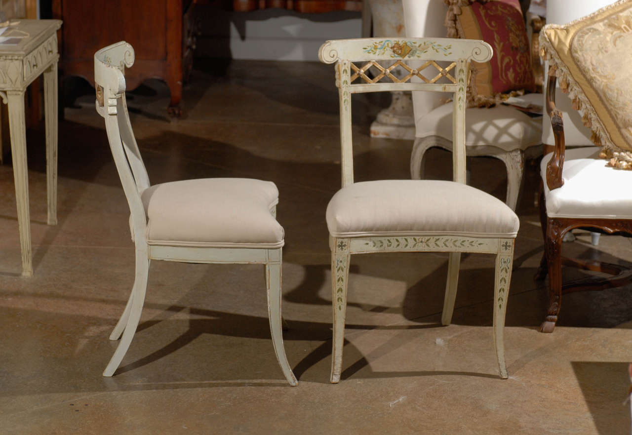 A Set of four Italian Neoclassical period painted wooden music chairs from the late 18th century with new upholstery. Each chair features a curved back, delicately accented by volutes on the sides, painted motifs on the upper rail and a gilded