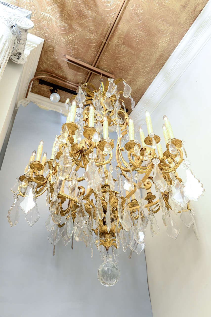Monumental thirty-six light chandelier, of gilt bronze, in the Brighton Pavilion style; its finely chased standard emanating clusters of scrolling foliate candlearms at graduating heights, all elaborately dressed by rosettes, pendants, and scallops