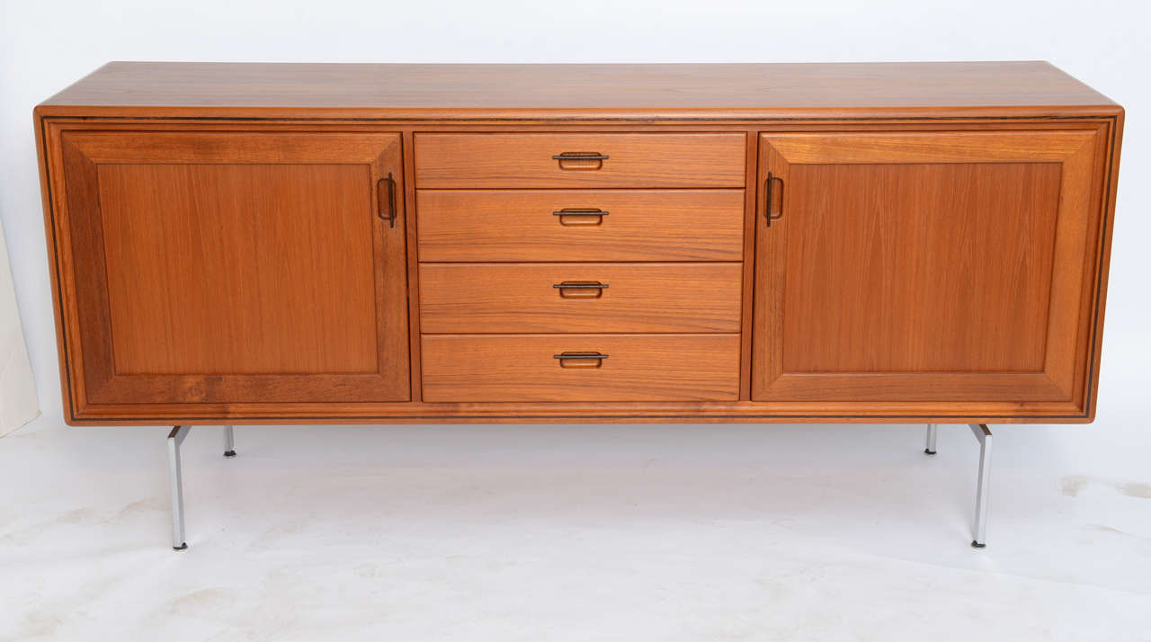 Outstanding Danish craftsmanship and style is exhibited in this credenza sideboard in warm figured teak with wenge wood pulls and inlay. Made by EMC Møbler it features four centered drawers with the top one felt lined. To the sides, doors opening to